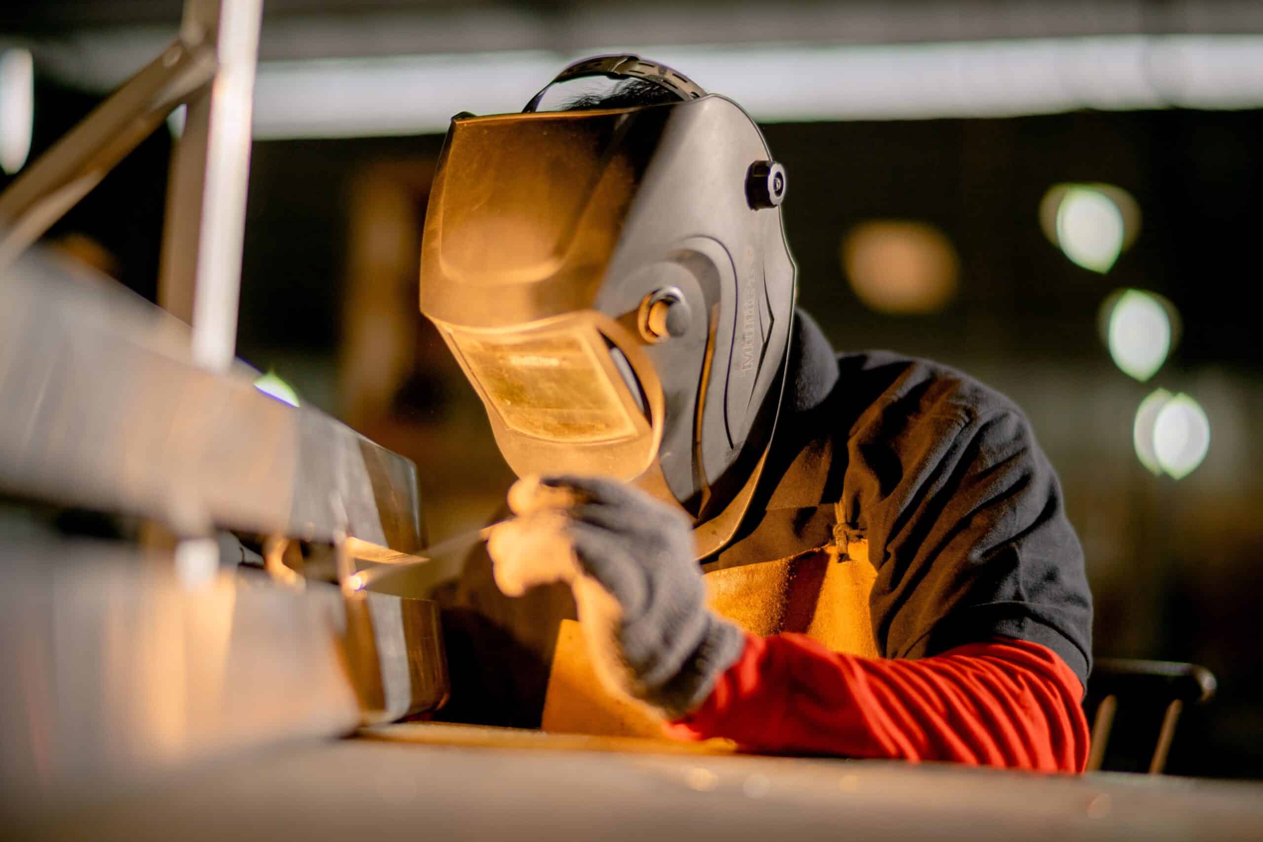 A man in a welding mask working on some machinery.